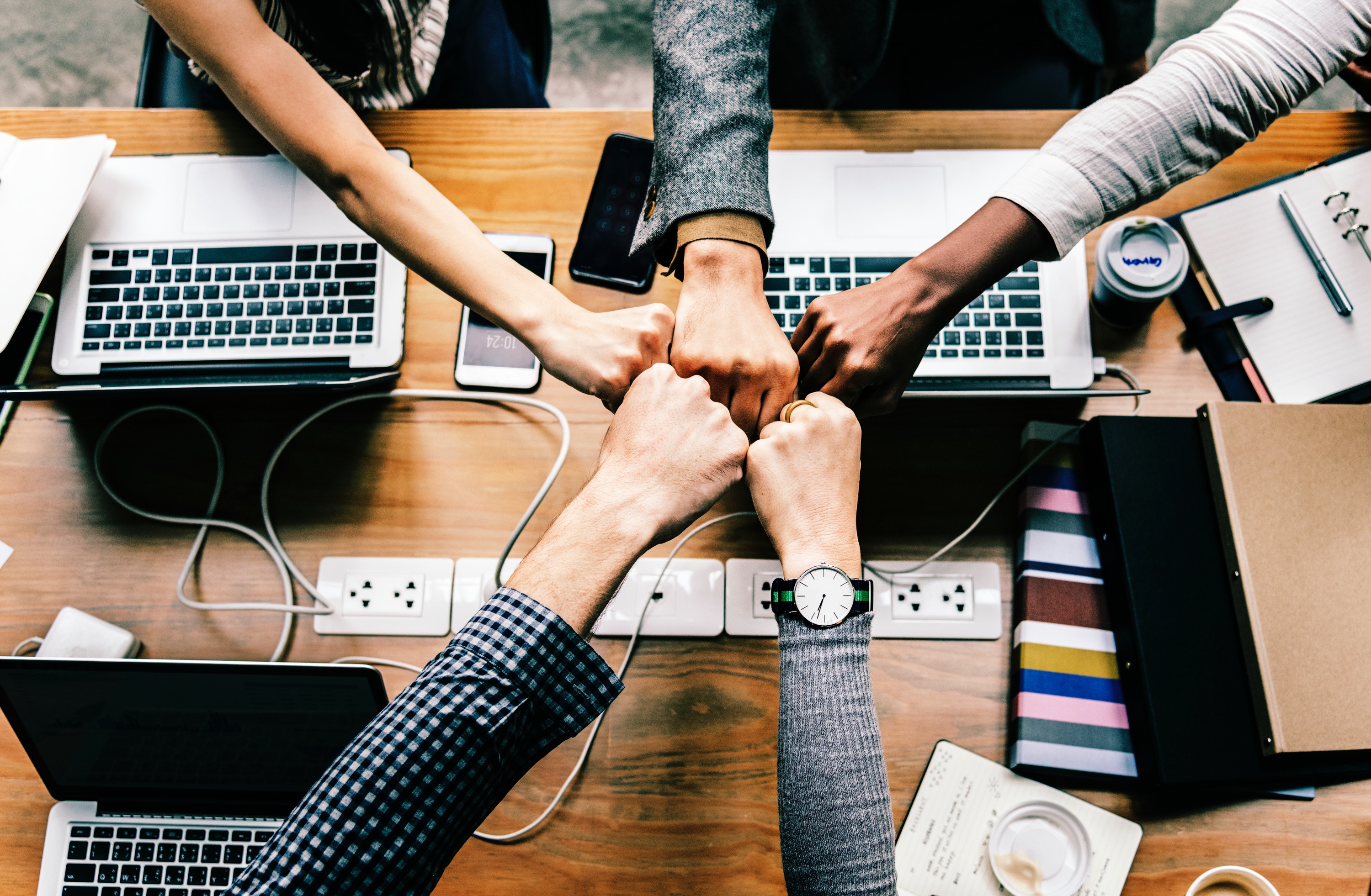 group of hands fist bumping over computers